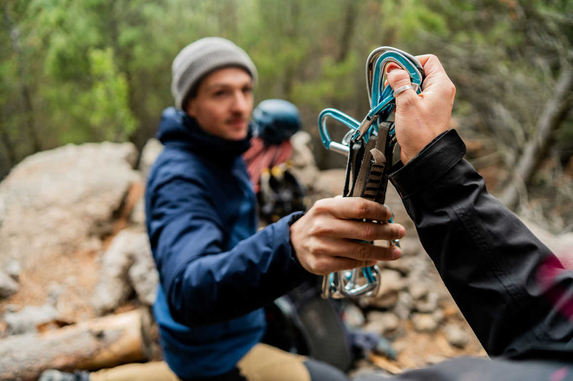 A person hands over climbing gear, such as carabiners and quickdraws, to another.