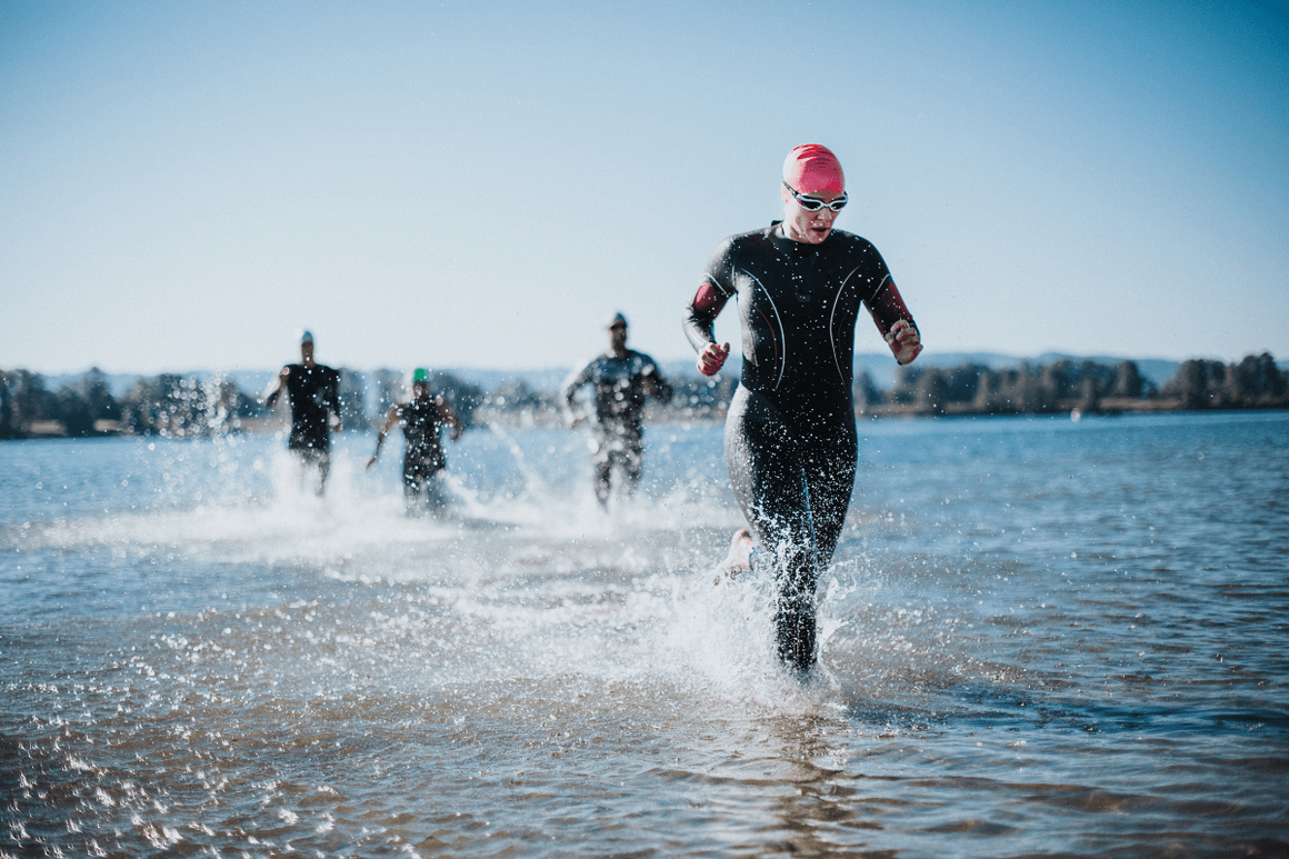 female coming out of lake after wild swimming in cap, goggles and swim suit