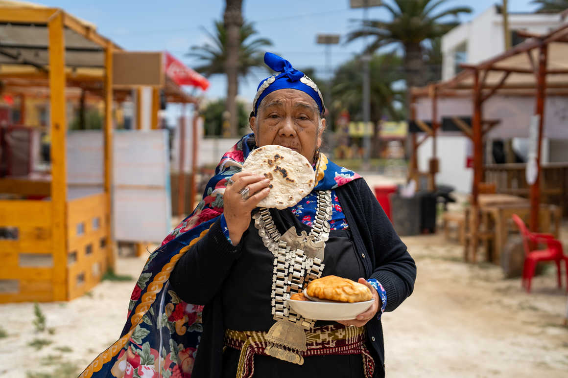 Indigenous mapuche woman in traditional dress and jewelry eating alipín bread
