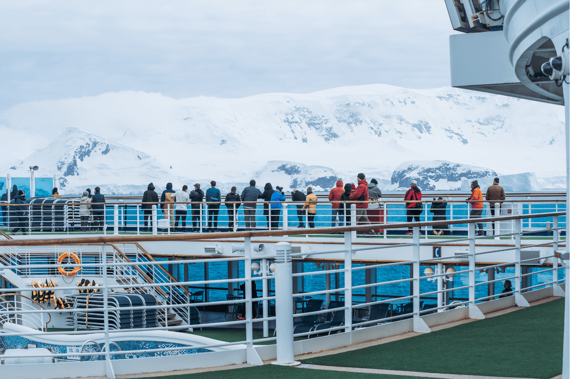 People on the deck of a cruise ship sailing past mountains of the Antarctic