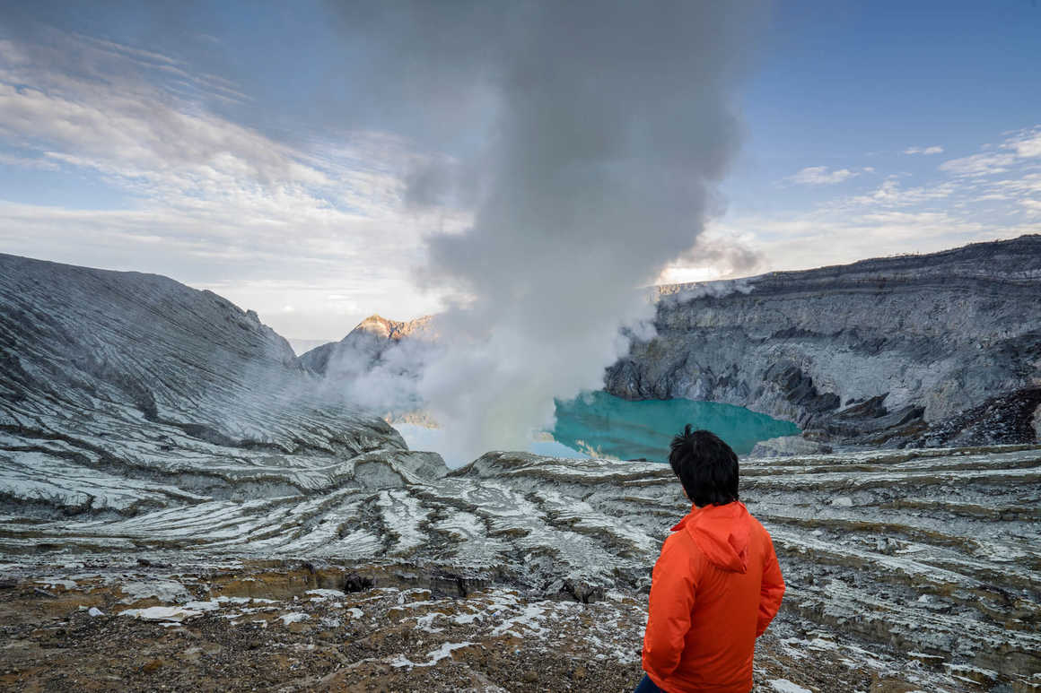 Traveller looking at crater blue lake at Kawah Ijen, Indonesia