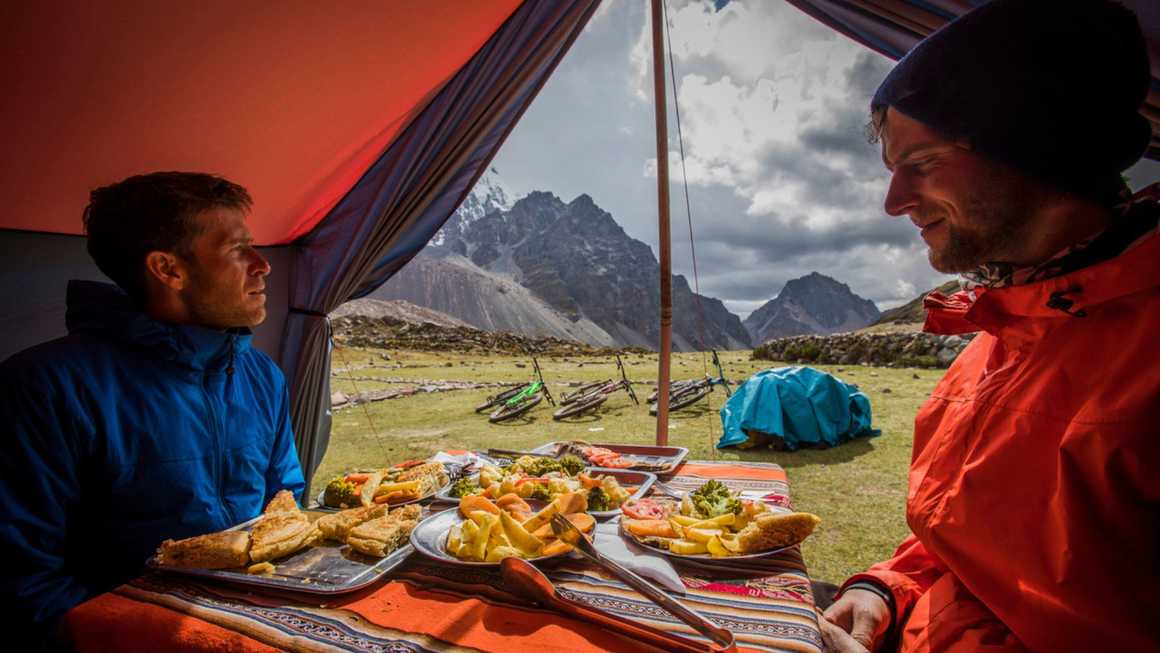 Two men in a tent enjoying food in the Andes, Peru