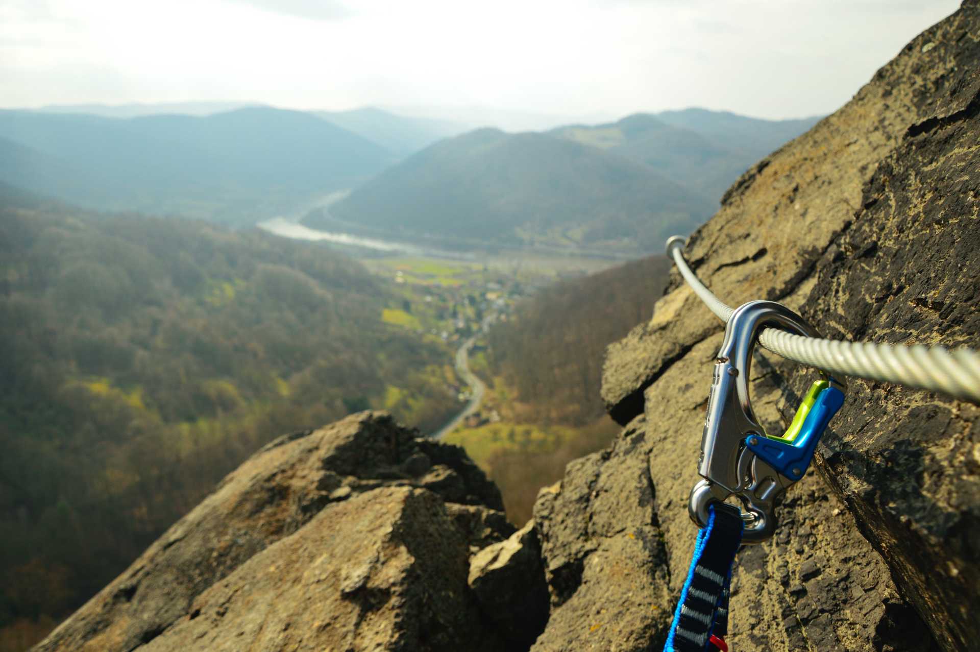 Carabiner clipped into steel wire across view of Italian mountains