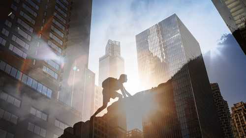 Man climbing a mountain with the backdrop of a city skyline
