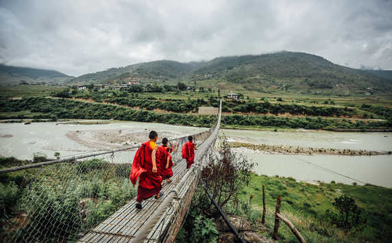 Young monks walking on a rope bridge in Bhutan